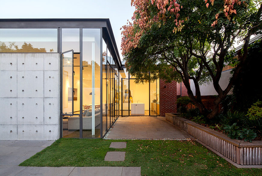 Here's a view of the rear side of the home, where we can take in the full breadth of the extension. This side is wrapped in full height glass, framed in steel, and anchored by a textural concrete wall at left. Here's a view of the rear side of the home, where we can take in the full breadth of the extension. This side is wrapped in full height glass, framed in steel, and anchored by a textural concrete wall at left.