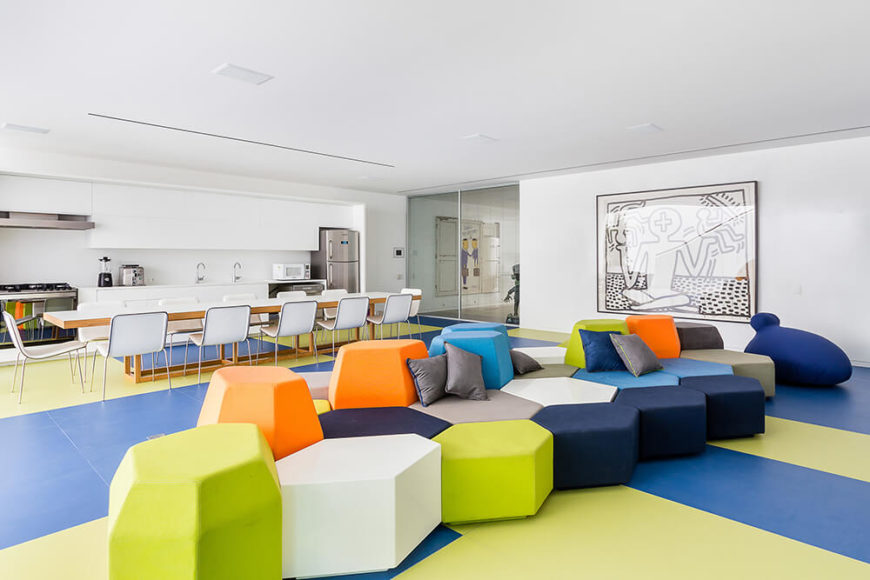 The massive, open plan center of the lower level is this vast play area, replete with geometric blocks in an array of colors over a two-tone set of flooring. The kitchen and lengthy dining table add a dose of function. To the right, we see a large Keith Haring painting. The massive, open plan center of the lower level is this vast play area, replete with geometric blocks in an array of colors over a two-tone set of flooring. The kitchen and lengthy dining table add a dose of function. To the right, we see a large Keith Haring painting.
