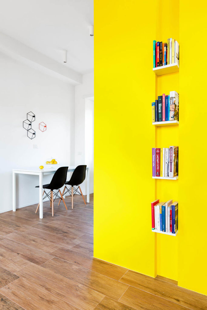 Along the bright yellow wall in the open plan space we see a series of small bookshelves, creating both a utilitarian and artistic flourish that adds a second layer of color and detail to the bright space. Along the bright yellow wall in the open plan space we see a series of small bookshelves, creating both a utilitarian and artistic flourish that adds a second layer of color and detail to the bright space.